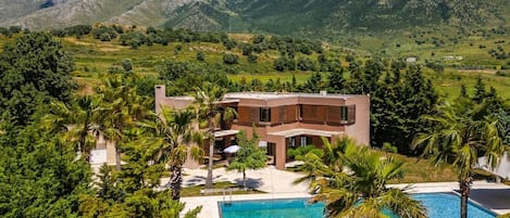 A modern house with a pool, surrounded by lush greenery and mountains.