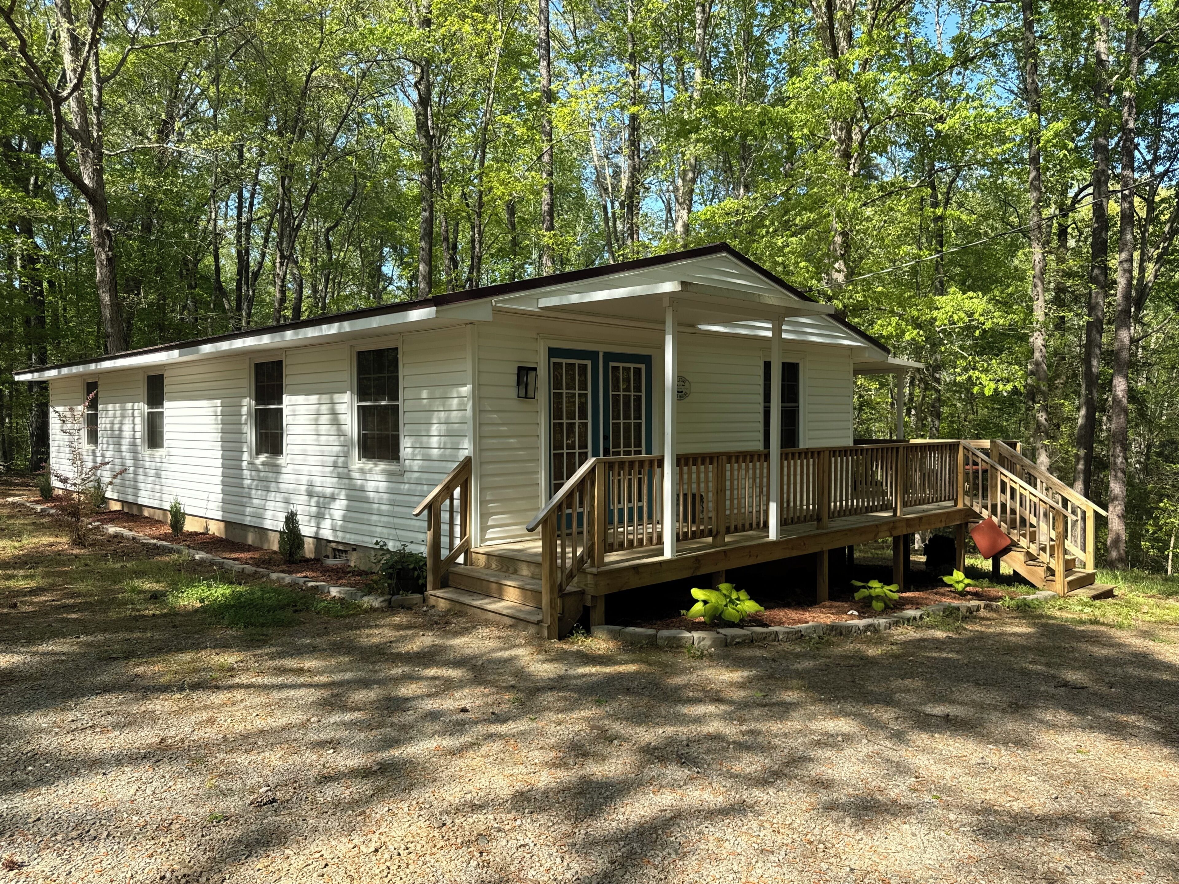 A single-story cabin with a front porch and a small deck, surrounded by trees.