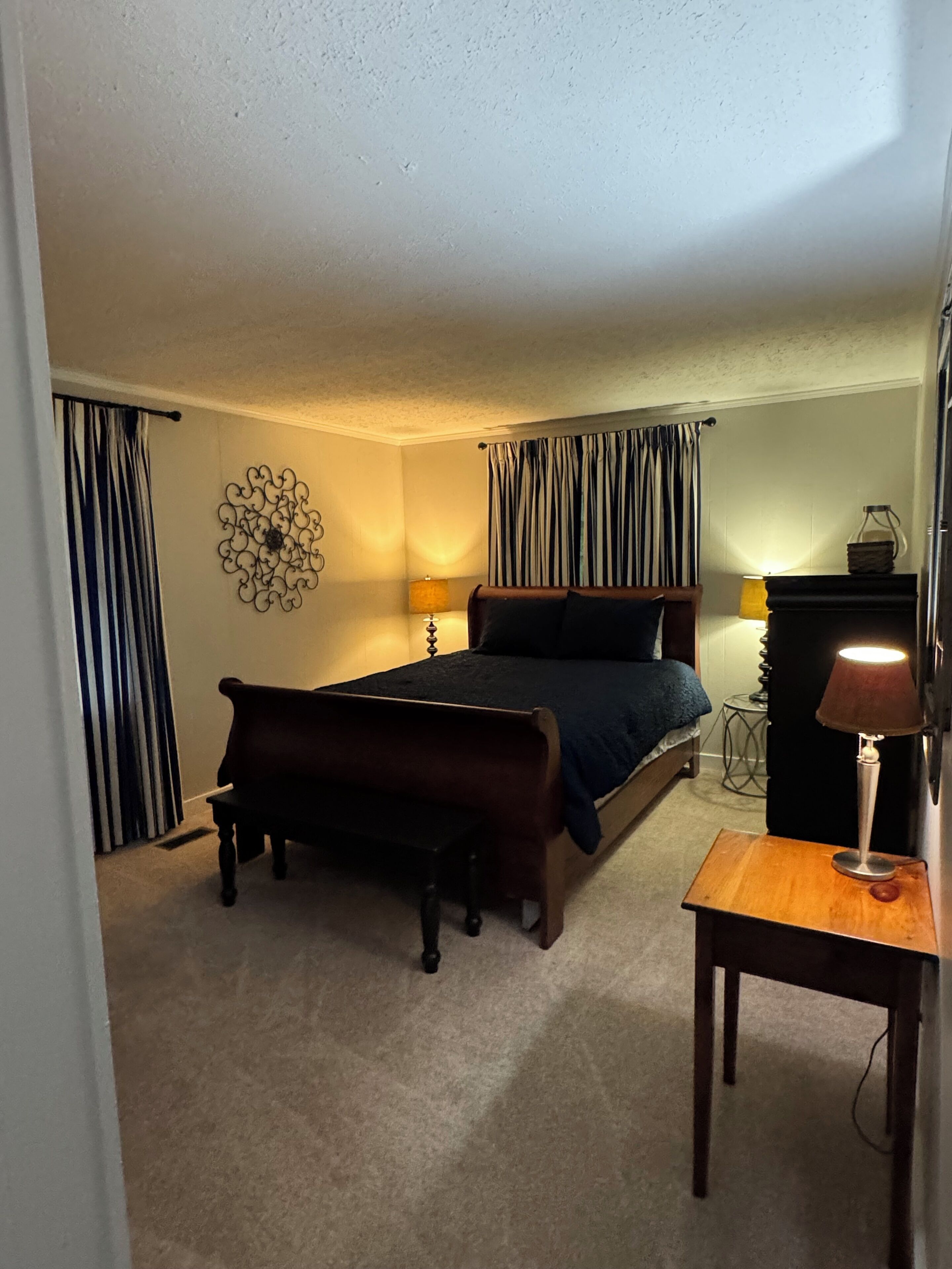 A bedroom with a bed, a bench, a lamp, and curtains.