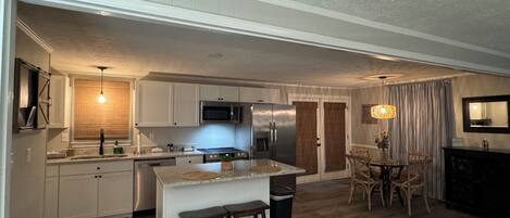 A modern kitchen with stainless steel appliances, a dining area with a chandelier, and a living space with a large window.