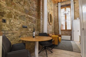 A stone-walled room with a round table, chairs, a sofa, a radiator, and a window with curtains. - Authentic Studios Alzazaba (Malaga)