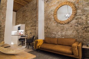 A living room with a brown sofa, a round mirror, a dining area with a table and chairs, and a kitchen in the background. - Authentic Studios Alzazaba (Malaga)