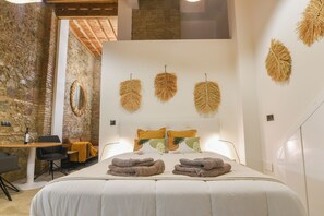 A hotel room with a bed, a small table with chairs, a stone wall, and decorative wall hangings. - Authentic Studios Alzazaba (Malaga)