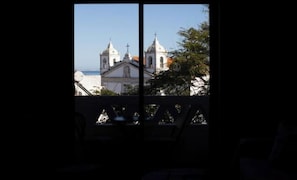 Blick durch ein Fenster mit Balkon, zeigt ein Gebäude mit zwei Kuppeln und einem Kreuz.