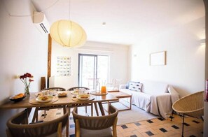 Ein Essbereich mit einem für das Frühstück gedeckten Tisch, einem Bett mit weißer Tagesdecke und einem Korbstuhl.
