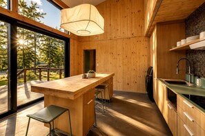 A modern kitchen with wooden cabinetry, a bar area, and a view of the outdoors. - Serene Modern Tiny Home with Fiery Gizzard Reservoir Views Near Tracy City | Tennessee (Tracy City)