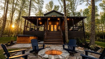 A cabin with a stone fire pit, two Adirondack chairs, and a staircase leading to the entrance.