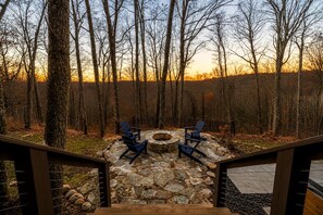 Un foyer en pierre, entouré de fauteuils Adirondack, situé dans une zone boisée.
