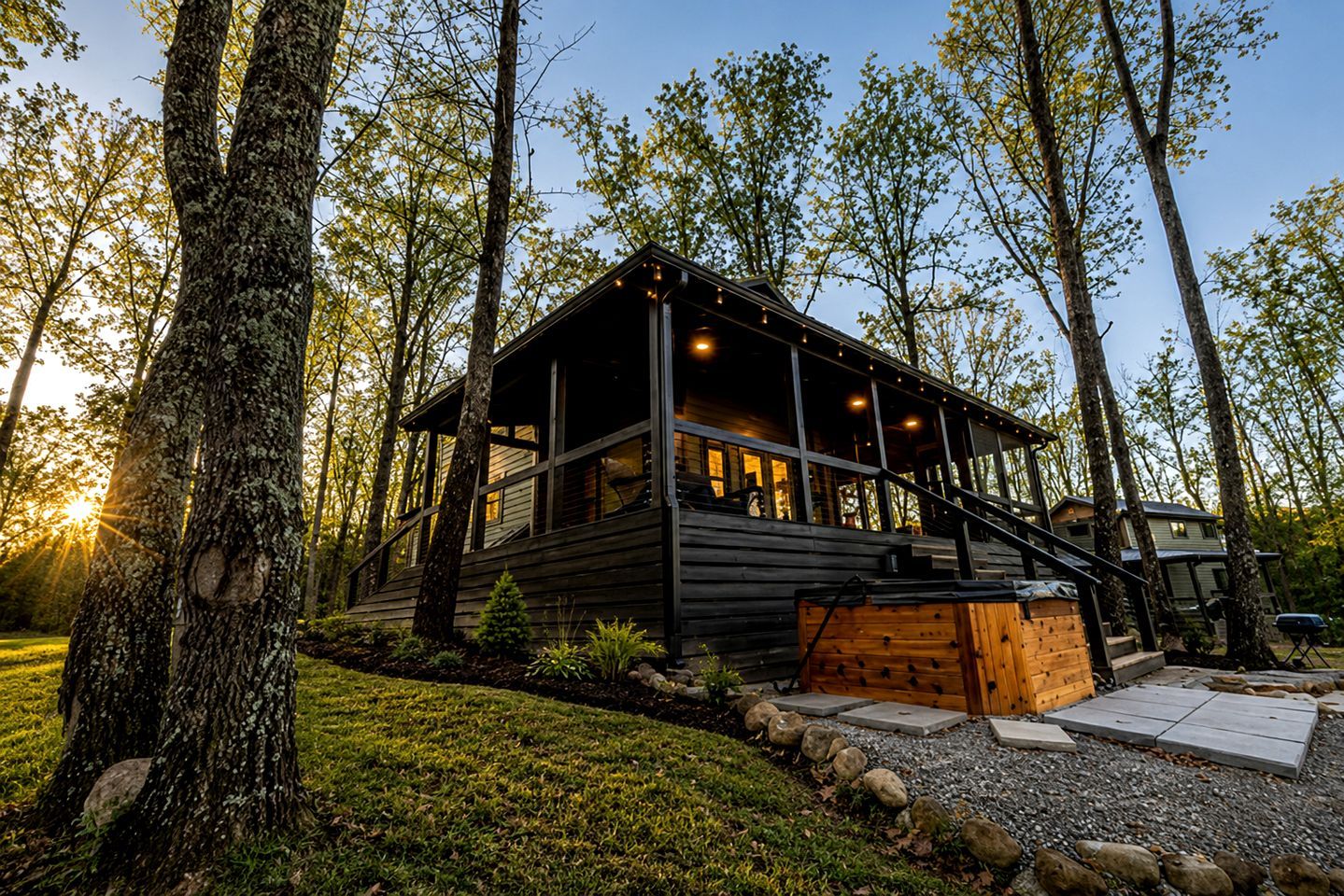 Une cabane dotée d’une terrasse, entourée d’arbres, et un chemin de gravier menant à l’entrée.