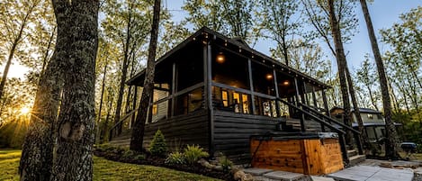 A cabin with a deck, surrounded by trees, and a gravel path leading to the entrance.