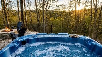A hot tub with a waterfall feature, surrounded by a stone fire pit and outdoor seating.