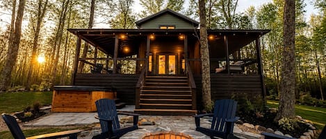 Una cabaña con un hogar de piedra, dos sillas Adirondack y una escalera que lleva a la entrada.