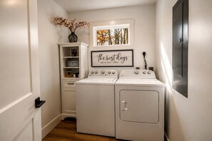 Une buanderie équipée d’un lave-linge et d’un sèche-linge, d’une étagère pour le rangement et d’un tableau encadré au mur.