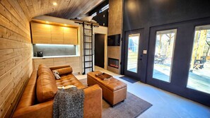 A modern interior with a wooden ceiling, a sofa, a coffee table, a fireplace, and large windows. - Retro Camper Retreat with Firepit & Hot Tub Escape in Sevierville, Tennessee (Sevierville)