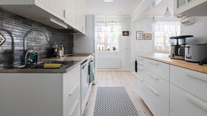 A modern kitchen with white cabinets, a black backsplash, and a window with sheer curtains. - Brunkulla - Tänndalen (Tänndalen)