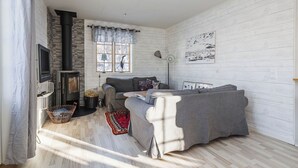 A cozy living room with a fireplace, a sofa, a TV, and a window with curtains. - Brunkulla - Tänndalen (Tänndalen)