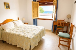 A bedroom with a bed, a desk, a chair, a window with a view of the sea, and a picture on the wall. - Magdalena 1st. Spacious apartment in the center of La Herradura bay (Almuñécar)