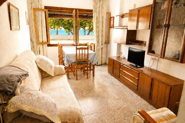 A living room with a sofa, dining table, chairs, a TV, and a view of the sea. - Magdalena 1st. Spacious apartment in the center of La Herradura bay (Almuñécar)