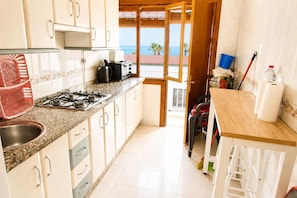 A kitchen with a gas stove, cabinets, a view of the ocean, and a dining area with a table and chairs. - Magdalena 1st. Spacious apartment in the center of La Herradura bay (Almuñécar)
