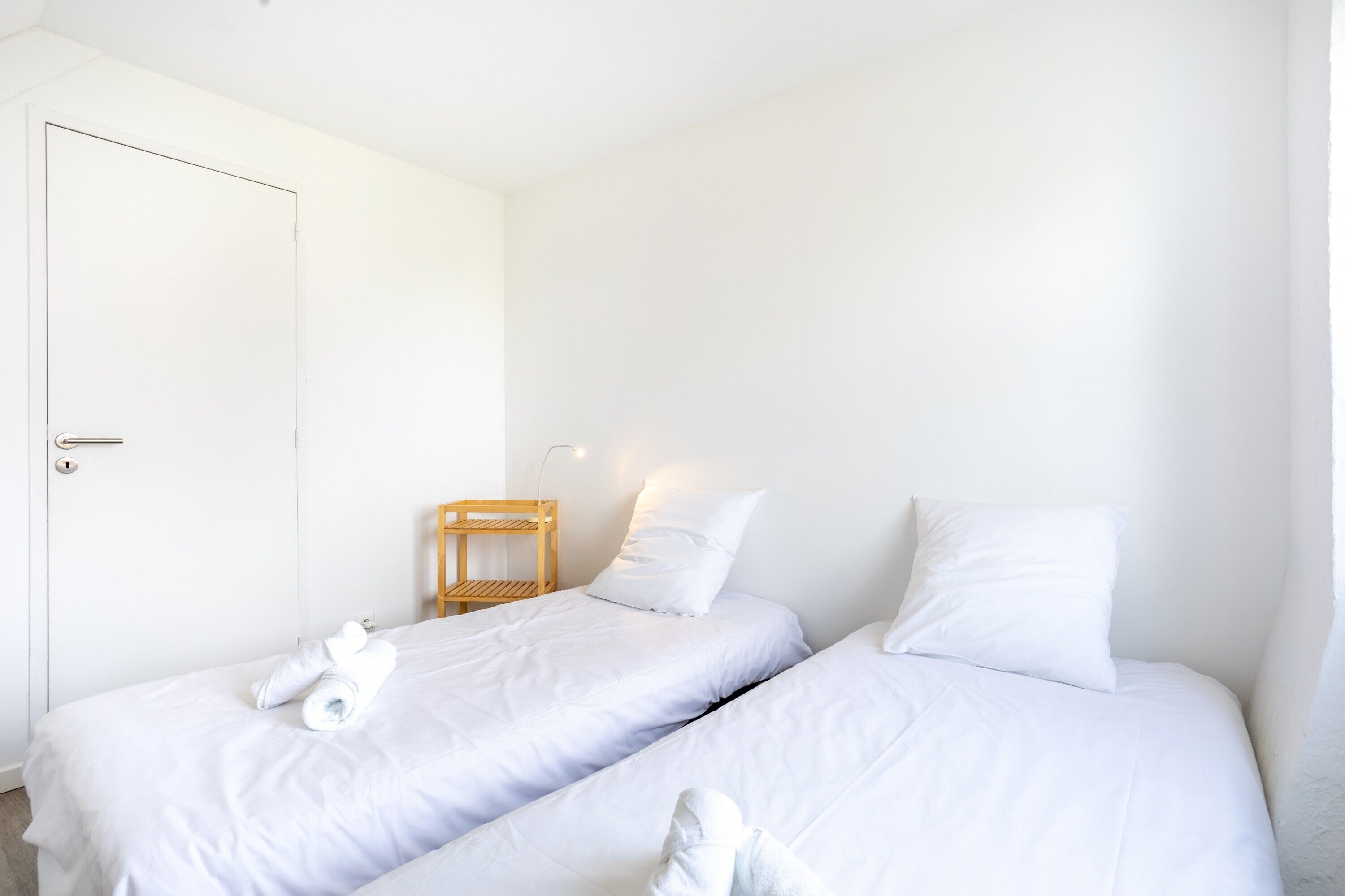 Een kamer met twee bedden, een houten stoel en een witte deur.
