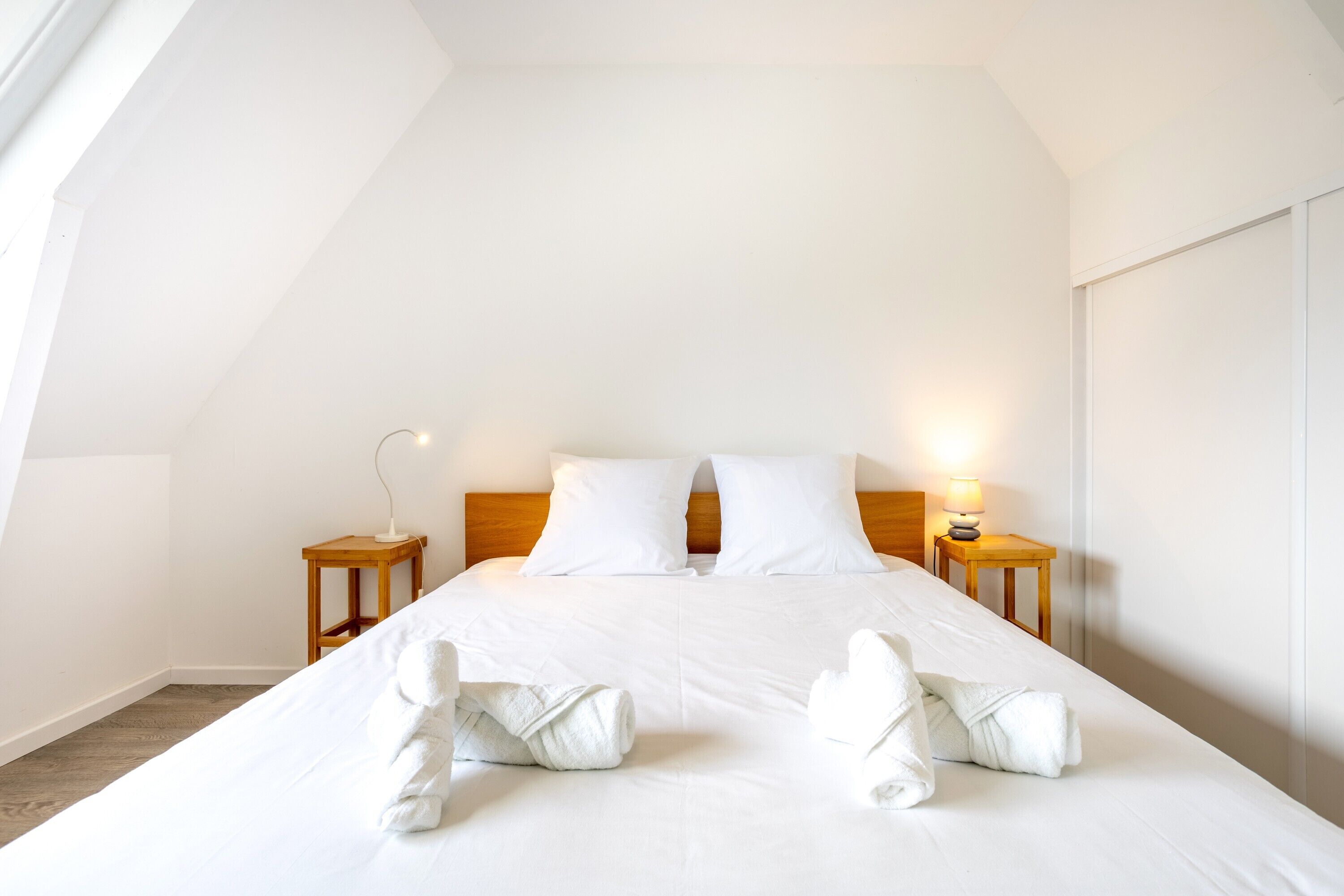 A bedroom with a large bed, two bedside tables, and a nightstand with a lamp.