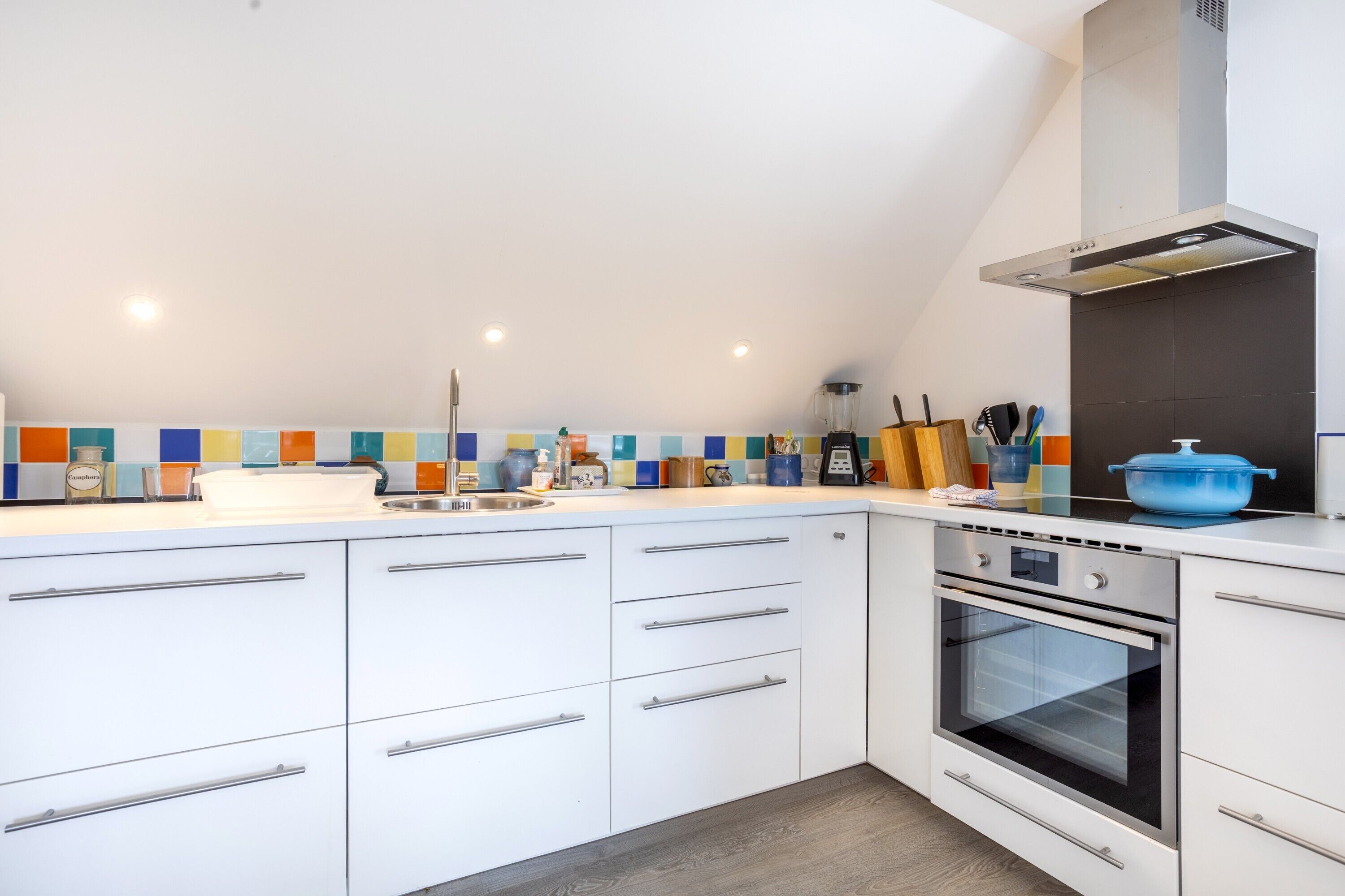 A modern kitchen with white cabinets, a built-in oven, and a colorful backsplash.