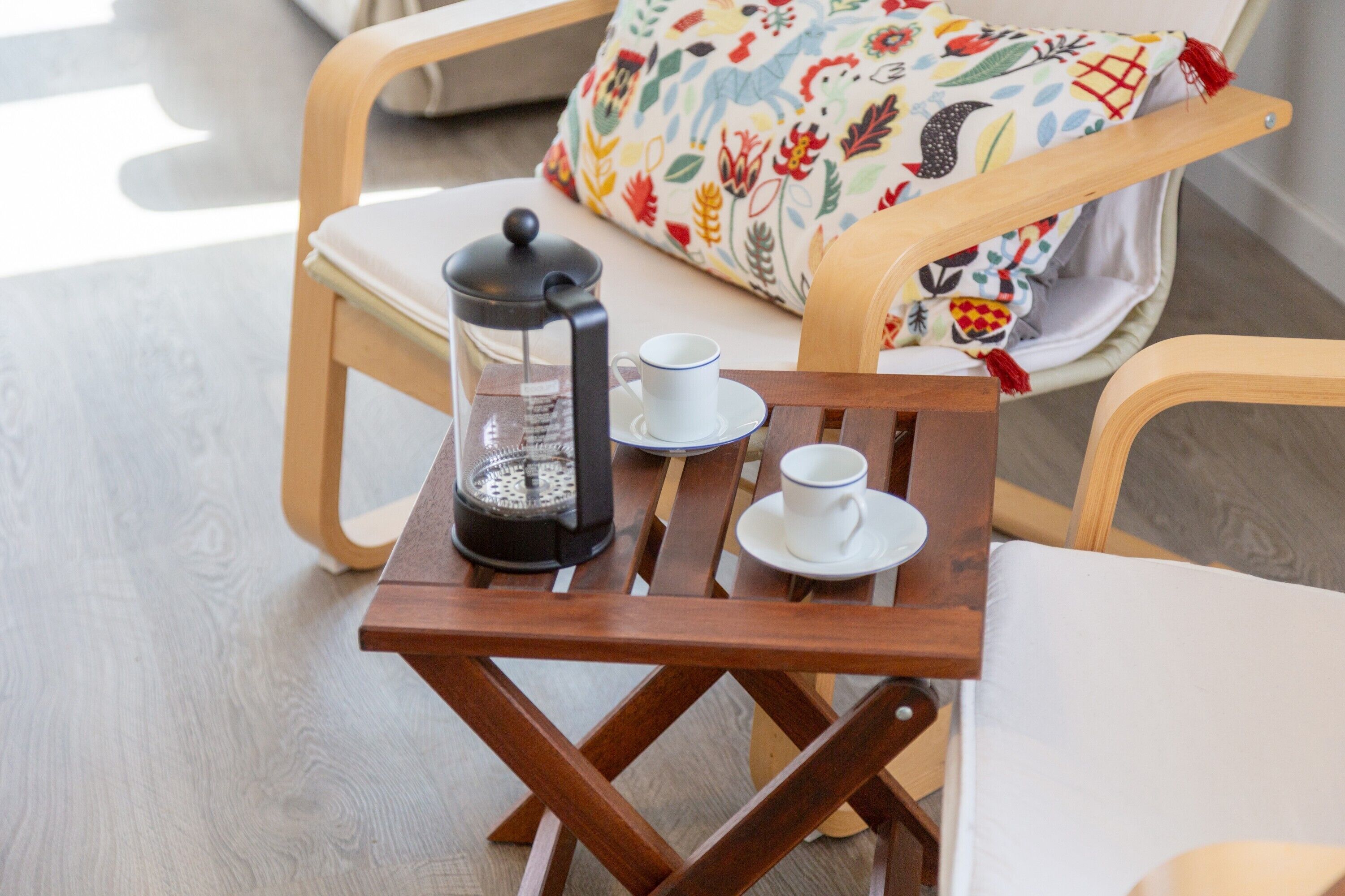 Una pequeña mesa de madera con una cafetera, dos tazas y un plato.