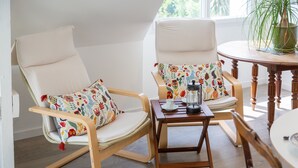 Une pièce avec deux fauteuils à bascule, une petite table sur laquelle se trouve une théière et une plante en pot.