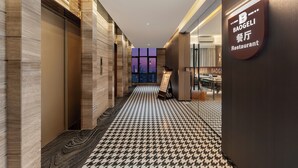 Un pasillo de hotel con suelo estampado, un cartel que indica un restaurante y vistas de la ciudad a través de la ventana.