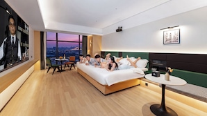 Una habitación de hotel moderna con una cama grande, una mesita pequeña, vistas a la ciudad y un proyector montado en la pared.