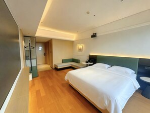 Een moderne hotelkamer met een groot bed, een zithoekje, een nachtkastje en een wandlamp.