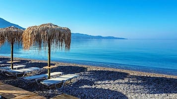A beach with lounge chairs and thatched umbrellas.