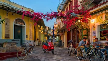 Una calle estrecha flanqueada por edificios, bicicletas estacionadas a lo largo de la acera y personas cenando en mesas al aire libre.