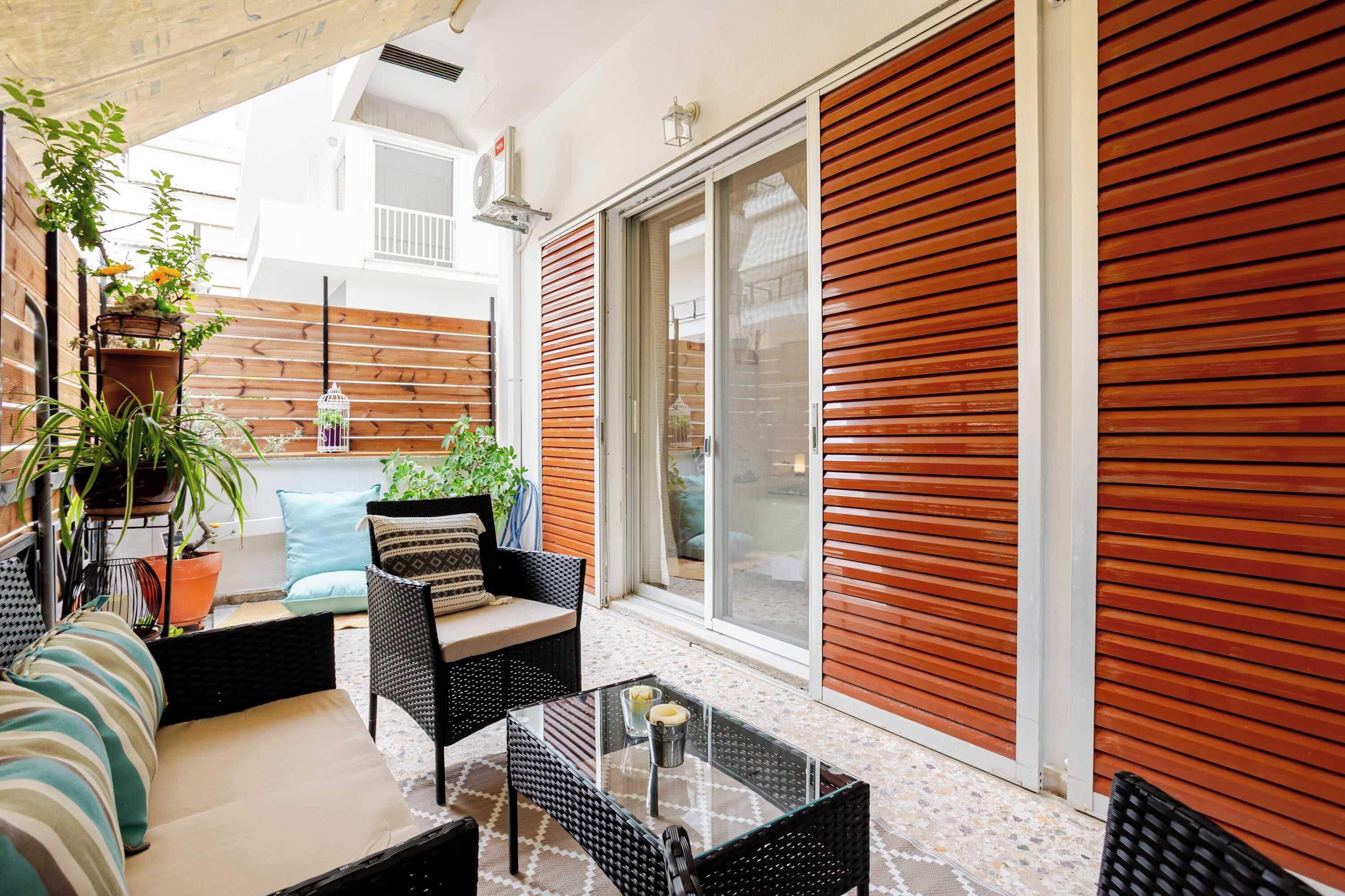 A patio with wicker furniture, a glass table, and potted plants.