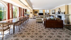 A spacious room with a large wooden dining table, comfortable seating, a fireplace, and large windows.