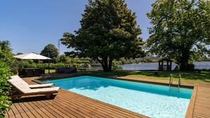 A swimming pool with wooden deck, lounge chairs, and a gazebo.