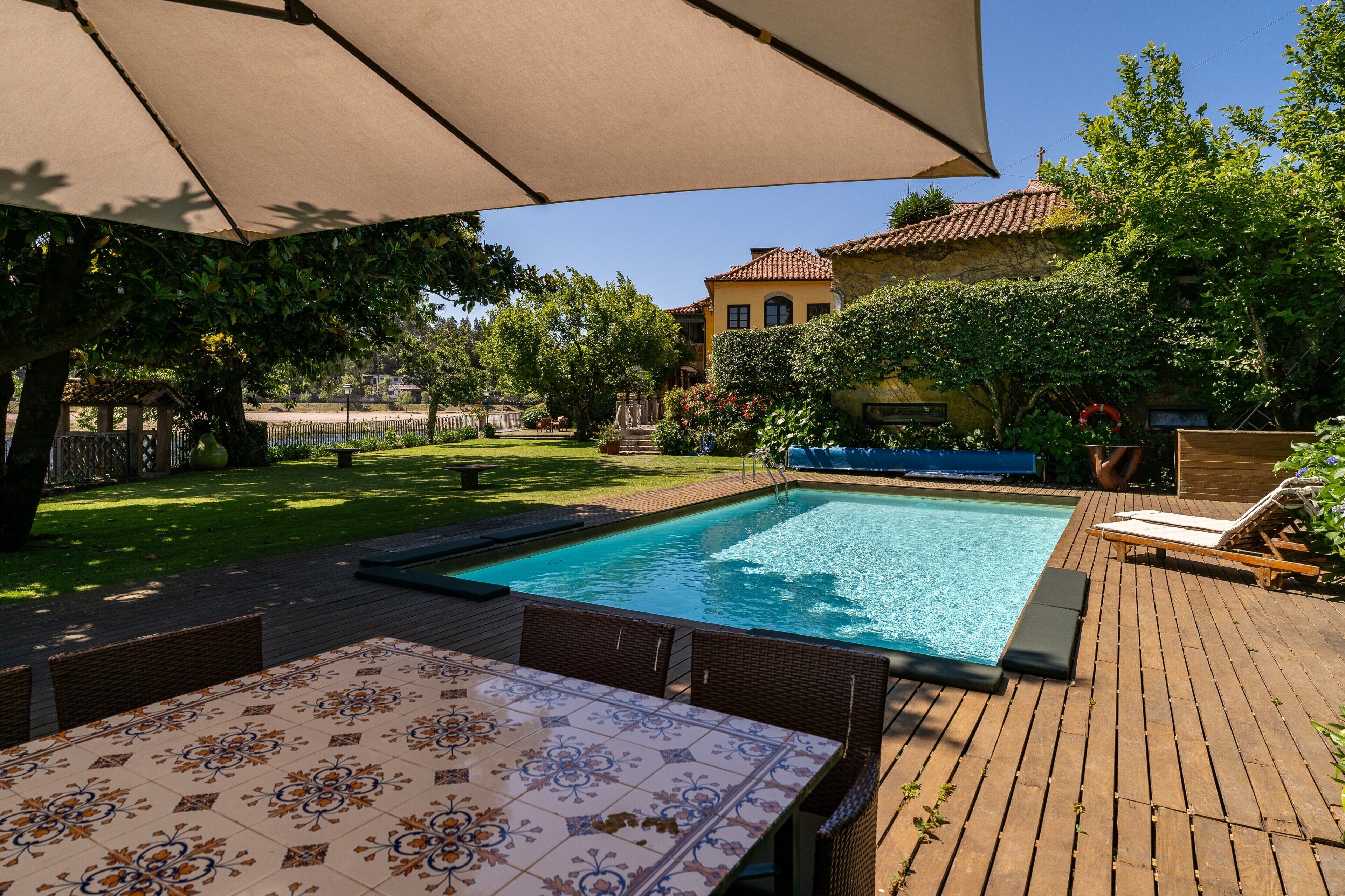 A pool area with a table and chairs, surrounded by a wooden deck and a large umbrella.