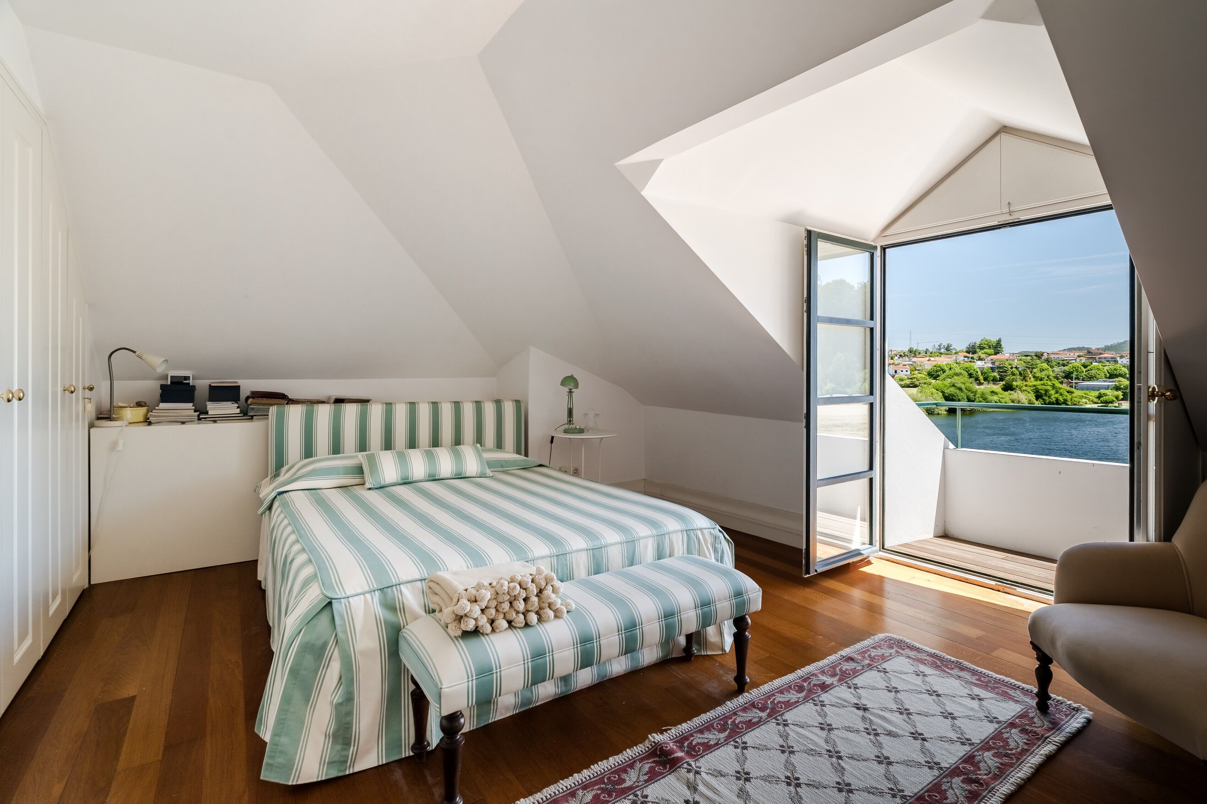 Un dormitorio con cama, mesita de noche, lámpara y vista a un cuerpo de agua.