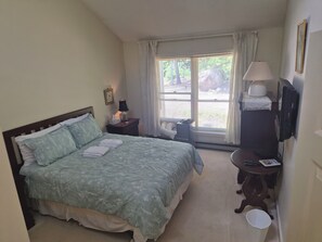 Ein Hotelzimmer mit Bett, Nachttisch mit Lampe, Fernseher und einem Fenster mit Vorhängen.