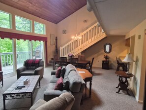 Ein geräumiges Wohnzimmer mit einer großen Couch, einem Couchtisch und einem Essbereich mit Stühlen und einem Tisch. Eine Treppe führt auf eine erhöhte Ebene.