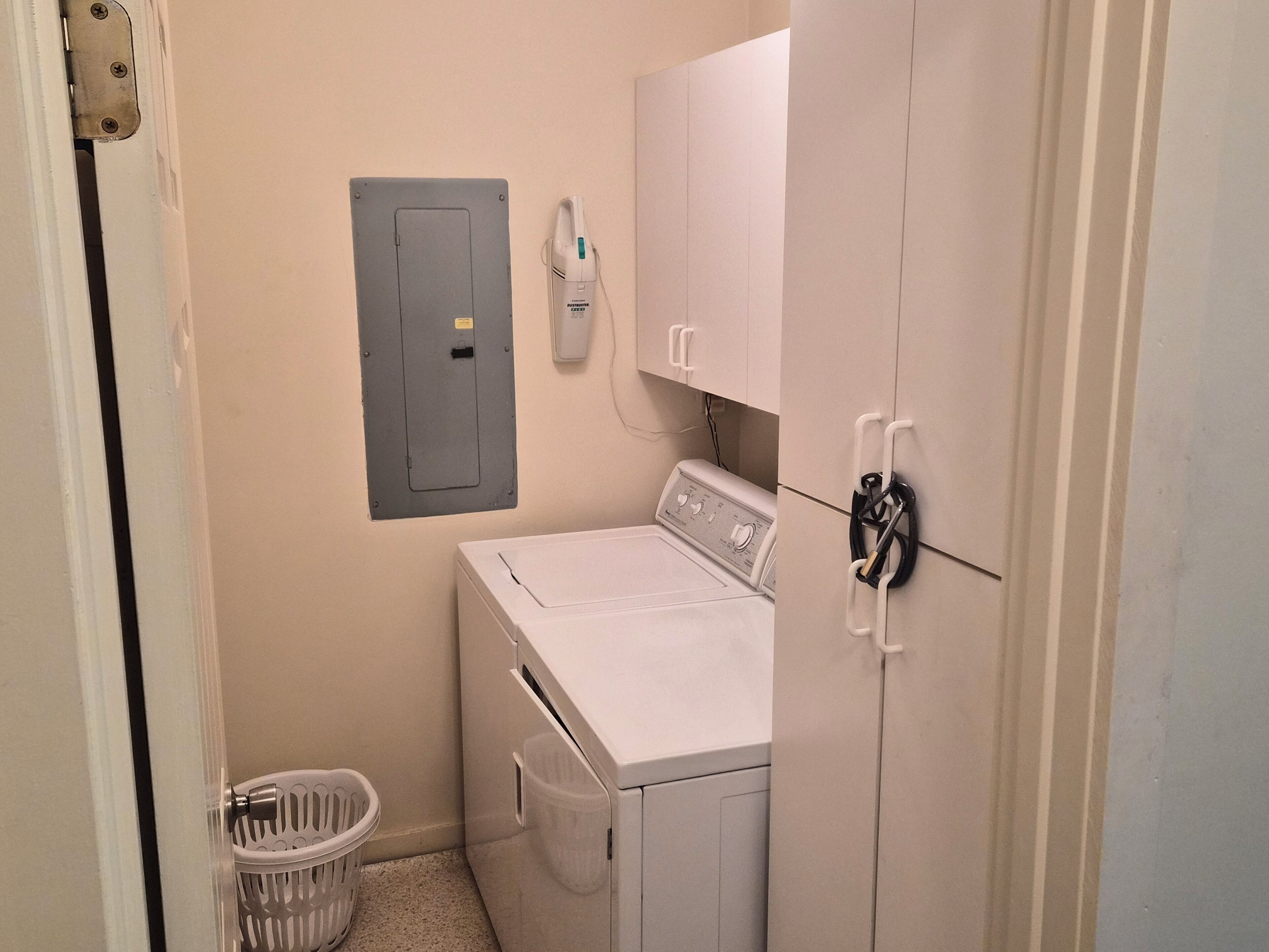 A laundry room with a washing machine, a dryer, a utility panel, and a trash bin.