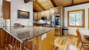 A kitchen with wooden cabinets, granite countertops, stainless steel appliances, and a bear-themed wall art. - Upscale Tahoe Townhome Near Incline w Fireplace (Incline Village)