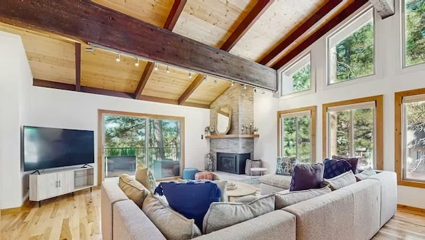 A spacious living room with a large sectional sofa, a flat-screen TV, a fireplace, and large windows offering a view of the outdoors. - Upscale Tahoe Townhome Near Incline w Fireplace (Incline Village)