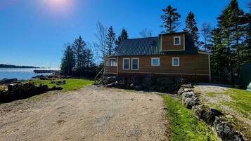 A wooden cabin with a metal roof, a gravel driveway, and a view of the water.