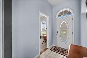 Ein Flur mit hellblauer Wand, einer weißen Tür mit dekorativem Glasfenster und einem gemusterten Teppich.