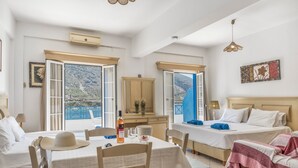 A hotel room with two beds, a dining table, and a view of the sea.