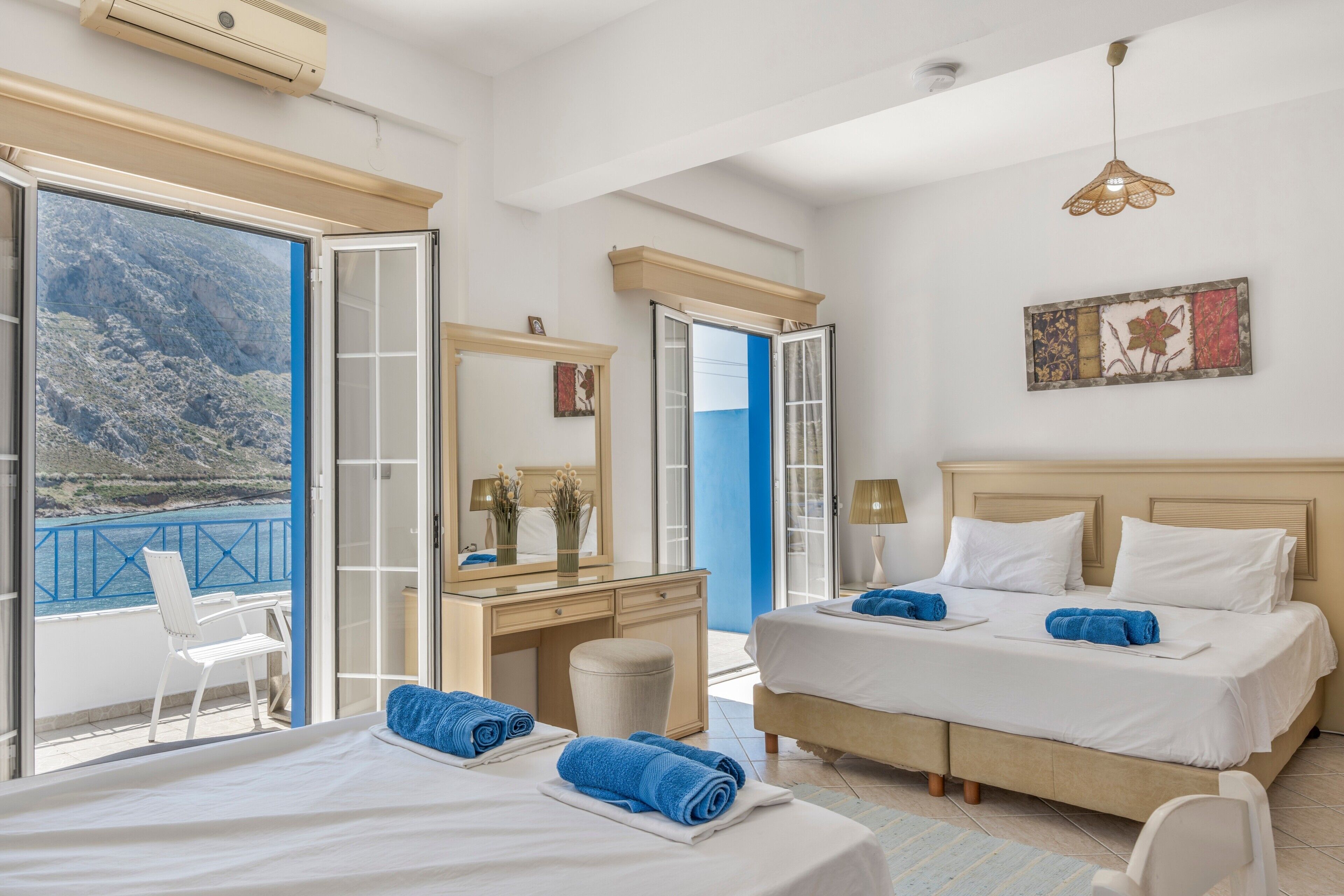 A hotel room with a bed, a desk, a chair, and a view of the sea.