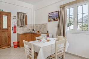 A kitchen with a dining table, chairs, a fire extinguisher, a window with a view, and a painting on the wall. - Katerina's Studio '1' with Sea View and Private Balcony (Arginonta)