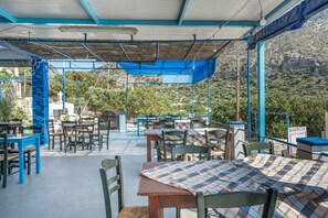 An outdoor dining area with tables and chairs, a covered section, and a view of a mountainous landscape. - Katerina's Studio '1' with Sea View and Private Balcony (Arginonta)
