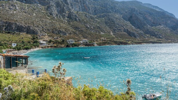 A coastal view with a mountain backdrop, clear turquoise sea, and a small boat.